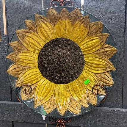 Garden CenterMetal sunflower art featuring a chocolate-brown inner circle and petals that transition from yellow to bronze tones. The sunflower is mounted on a blueish-grey base, adding a rustic and artistic touch.