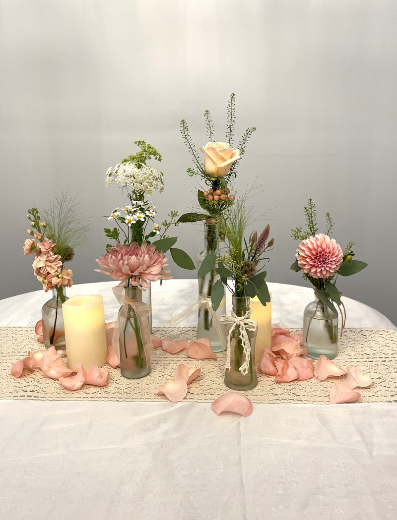 A variety of wedding floral arrangements, including lush centerpieces, elegant arch decor, free-standing ground installations, and delicate table accents. Featuring roses, peonies, wildflowers, and greenery, complemented by candles and soft lighting for a romantic ambiance.